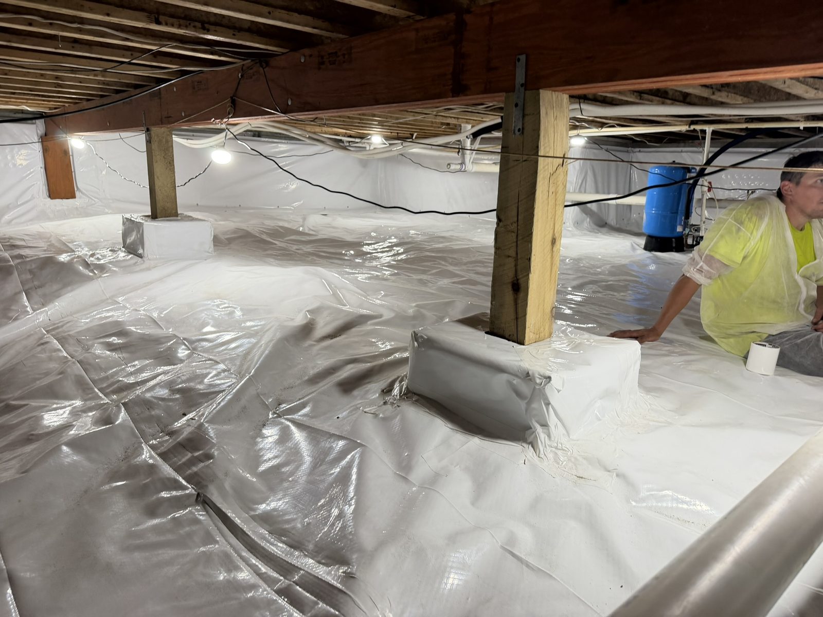 Completed crawl space encapsulation with sealed floor liner, wrapped support piers, and lined foundation walls