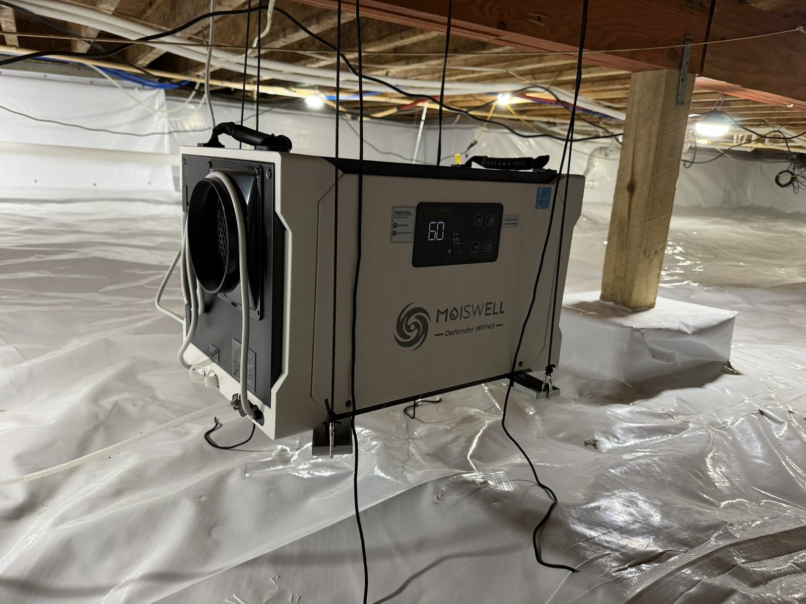 Crawl space dehumidifier installed and suspended from floor joists above an encapsulated crawl space floor